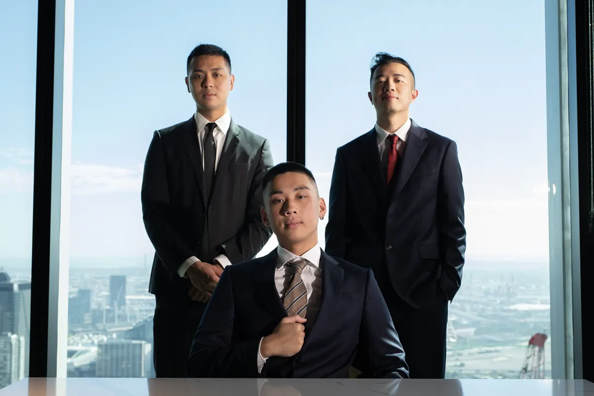 Stanley Ma and Terence Mok standing and Jordan Pham seated at a marble desk, in suits, in front of floor-to-ceiling windows over Melbourne.